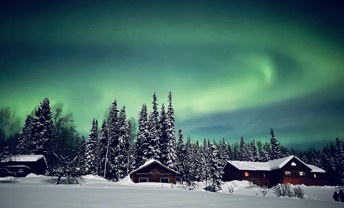Alaska Adventure Tours 6 Northern Lights Aurora Borealis in Alaska with snow covered trees and hut