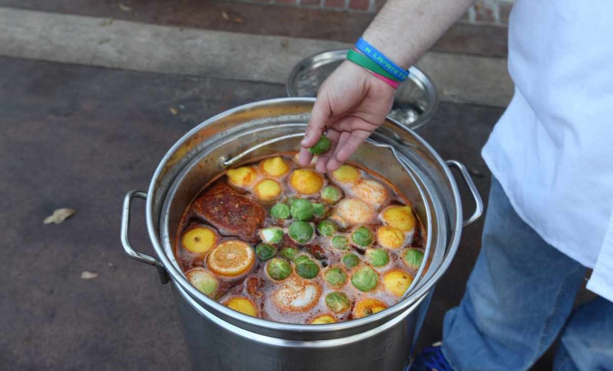 Exploring Louisiana: Be Transported to Another Country 3 Someone hand next to a a large pot containing a traditional Louisiana seafood boil